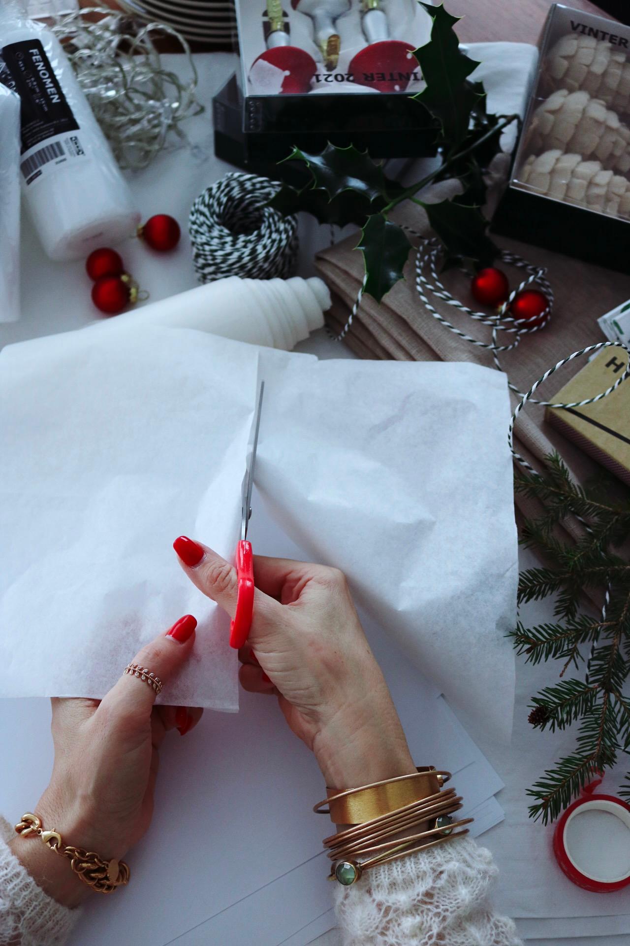 .Le mani di una donna tagliano un pezzo di carta velina bianca con le forbici.