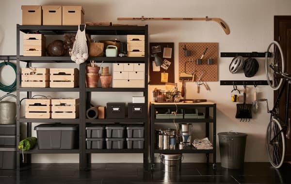 Le mur d’un garage avec une étagère BROR noire remplie de boîtes en bois, carton et plastique dans des dimensions variées.