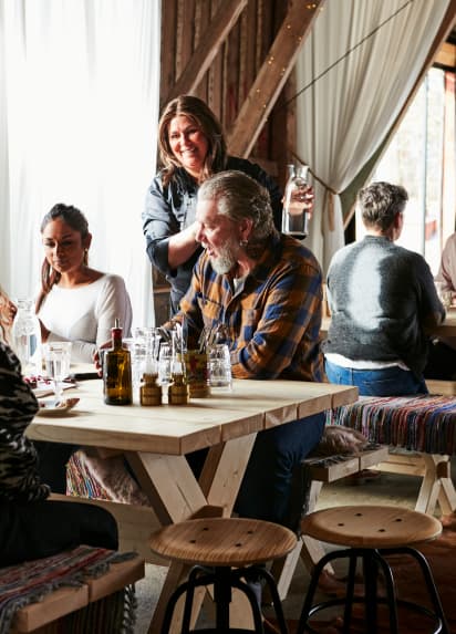 Les clients sont assis à une table en bois et discutent avec une serveuse.