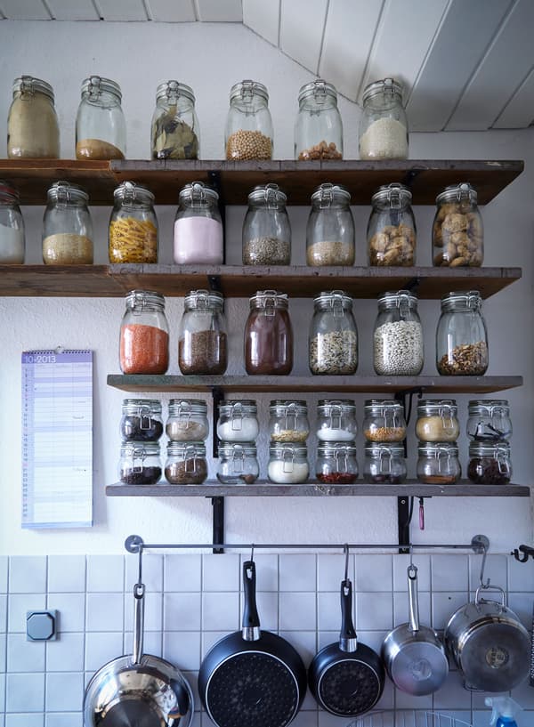 Les ingrédients secs sont exposés (et stockés) dans des bocaux assortis le long de tablettes en bois dans une cuisine blanche.