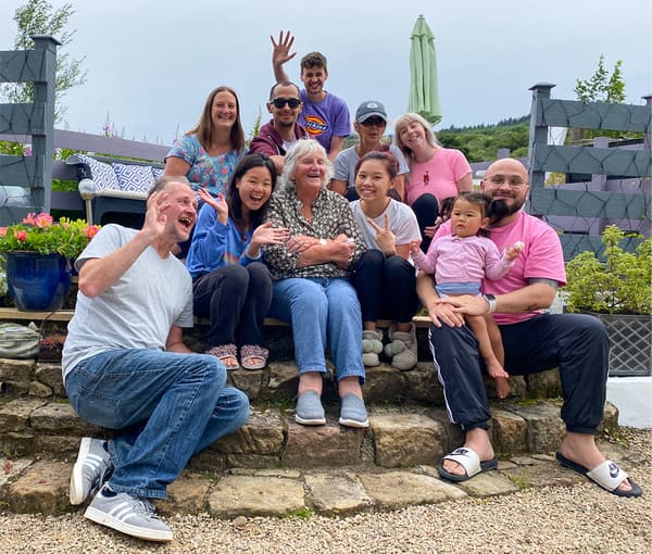 Les membres d'une famille sont assis ensemble à l'extérieur sur des marches en pierre, posant pour une photo. Ils ont le sourire et certains d'entre eux rient.