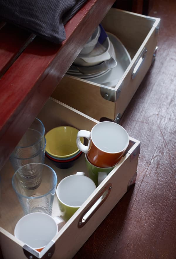 Les verres, mugs et autres articles de cuisine sont rangés dans des boîtes en bois sous un banc pour maximiser le rangement de la cuisine.