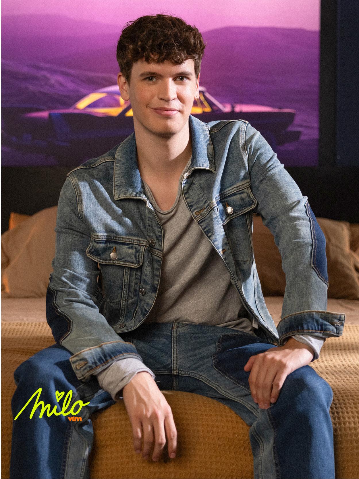 Liam in een denim outfit vormt een casual en moderne setting met een paarse achtergrond.