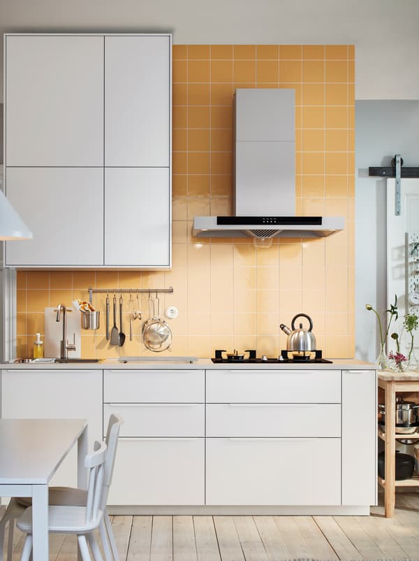 Light-brown tiled kitchen wall. Worktop with sink, hob and utensils, framed above and below by rows of white METOD cabinets.