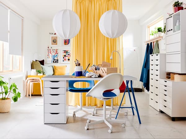 Light gray/white table with blue legs and drawer unit, three white/blue/red swivel chairs and yellow room-dividing curtains.