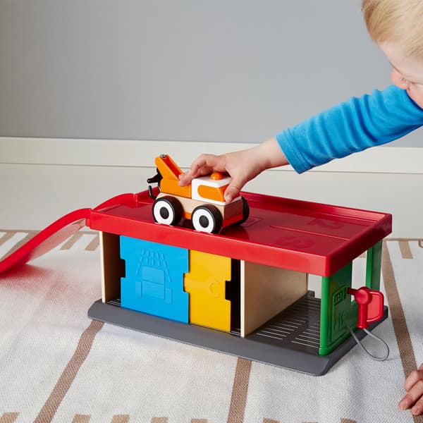 פעוט משחק על הרצפה עם מוסך LILLABO של איקאה ועם משאית גרירה.