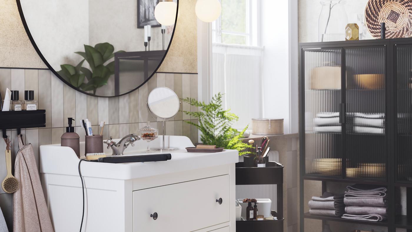 LINDBYN ogledalo visi iznad belog HEMNES/RÄTTVIKEN postolja umivaonika s dve fioke, pored FRIHULT zidne lampe.
