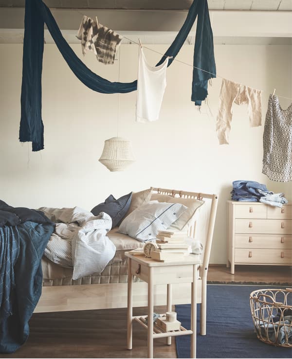 Linen hanging above a wooden bed frame, bedside table and chest of drawers.