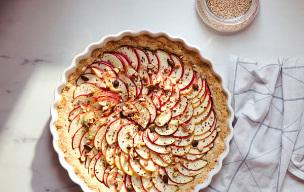 Linge à vaisselle blanc à rayures grises et tarte recouverte de fines tranches de pommes dans un moule à tarte blanc VARDAGEN.