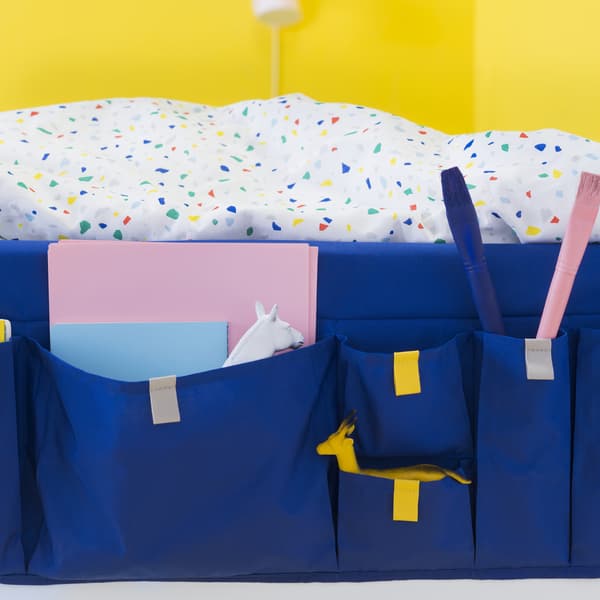 Linge de lit coloré et rangement à poches bleu pour le lit, garnies de carnets, sur fond jaune.