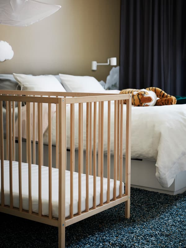 Lit à barreaux SNIGLAR en bois dans une chambre avec moquette, lit deux places, peluche tigre et rideaux opaques.