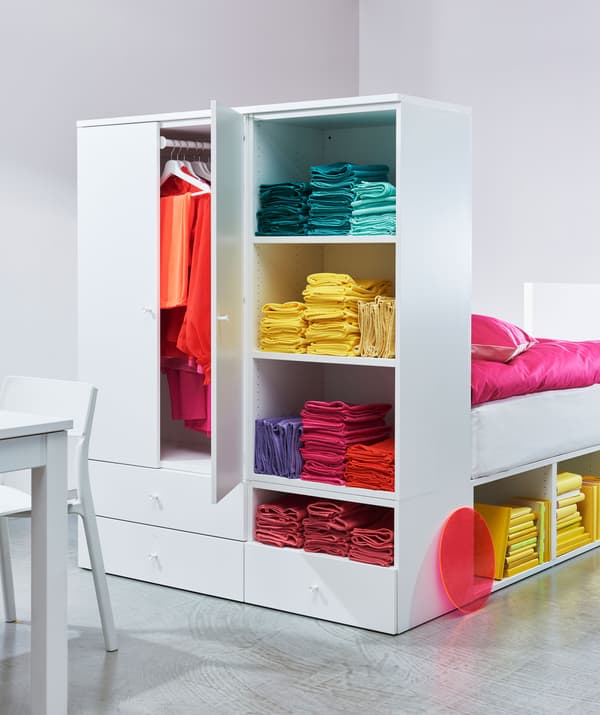 Lit avec garde-robe intégrée faisant office de tête de lit, dans laquelle sont rangés des vêtements multicolores.