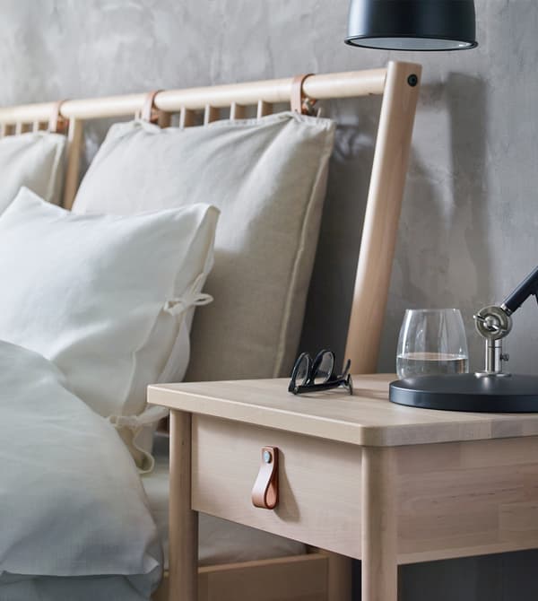 Lit avec parure blanche et table de chevet en bois dont le tiroir est doté d’une poignée en cuir.