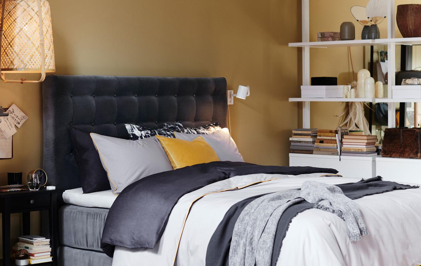 Lit avec tête de lit matelassée en velours gris et draps superposés.
