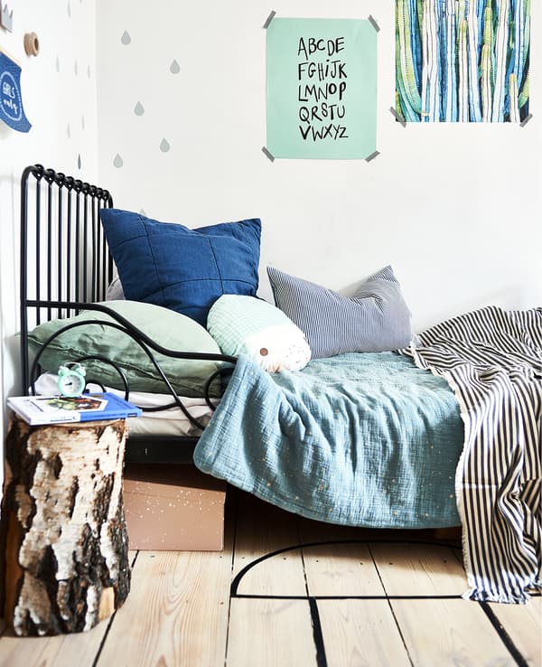 Lit en métal noir, linge de lit vert et bleu et affiches au mur.