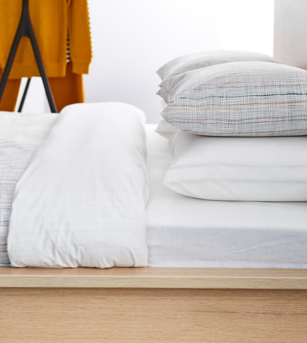 Lit impeccablement fait, vu de côté, avec linge blanc et oreillers ornés de rayures simples.