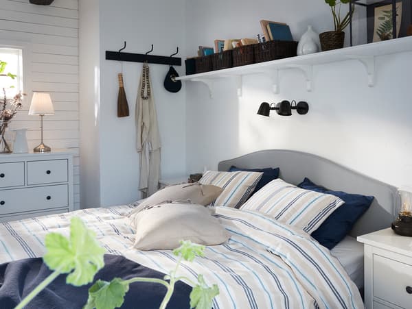 Lit matelassé IKEA HAUGA en beige, avec housse de couette et taies d’oreiller à rayures, surmonté par deux appliques noires.