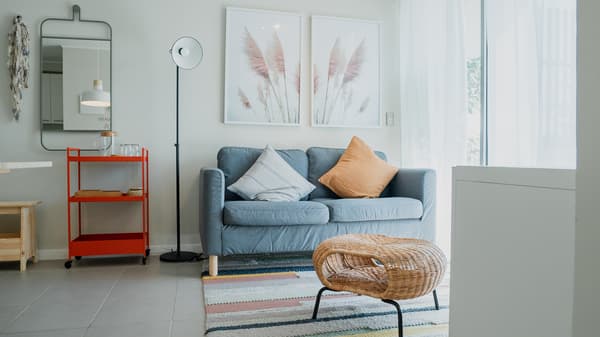 Living con sofa celeste de dos cueros con cojines naranjo y blanco con lineas. Frente a el una mesa de centro redonda sobre una alfombra.