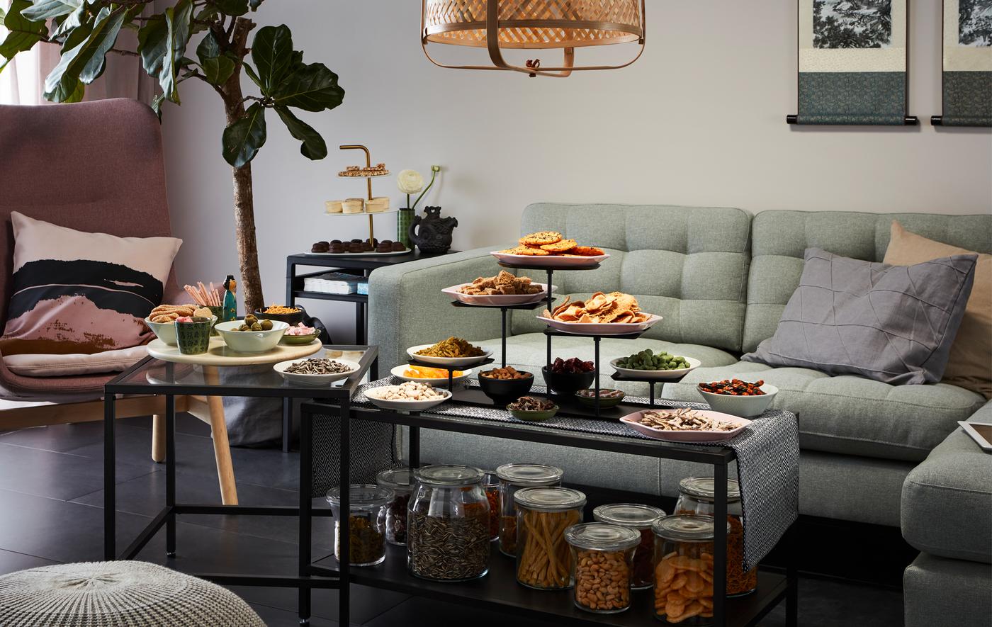 Living room side with corner sofa and armchair, fronted by a set of nest tables laden with snacks, both stored and served.
