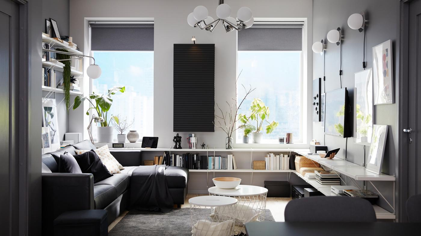 Living room with a black sofa-bed with chaise longue, white shelves, a wall-mounted cabinet and a dark grey rug.