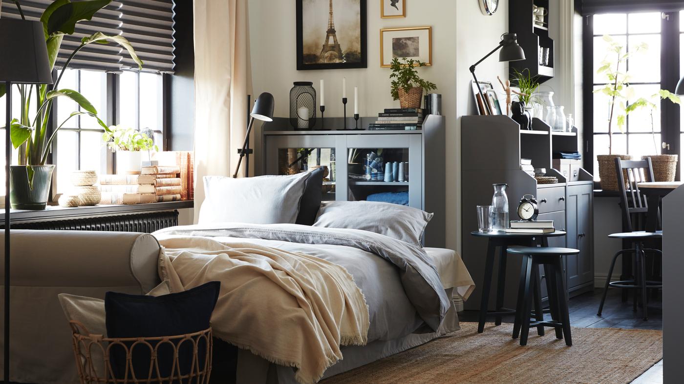 Living room with a light beige sofa-bed, a jute rug, a rattan/bamboo chair and two cabinets and a chest of drawers in grey.