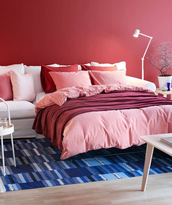 Living room with GRÖNLID sofa expanded to form a double bed, neatly made with volumes of fluffy bed textiles and cushions.