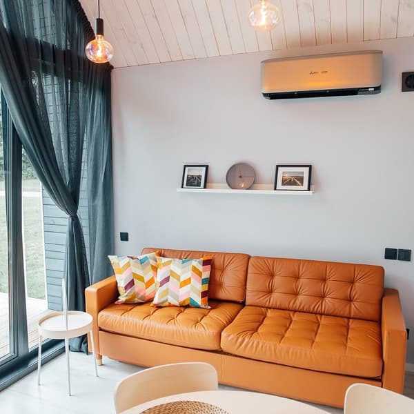 Living room with tan leather sofa and colorful pillows – Bright, modern lounge with a comfortable leather sofa, patterned cushions, and wall-mounted shelf with décor items.
