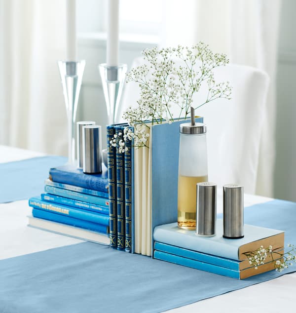 Livres bleus arrangés en centre de table, avec bougies, gypsophile, salière, poivrière et flacon à huile.