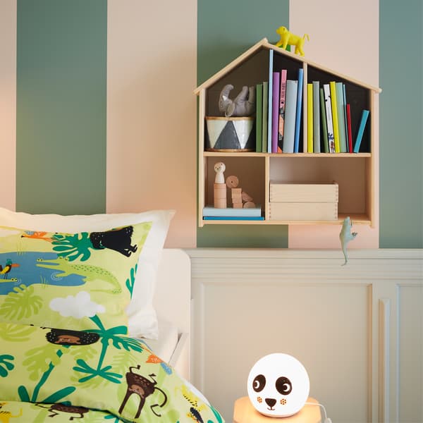 Livres dans une maison de poupées fixée au mur, literie à motifs jungle et lampe de table à motifs panda.
