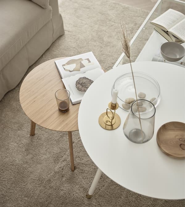 Looking down on two circular coffee tables, one white and one natural wood, in a living room.