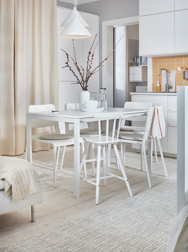 Lumineux et blanc, un appartement décoré d’une table MELLTORP et de chaises TEODORES entre une kitchenette et un lit.