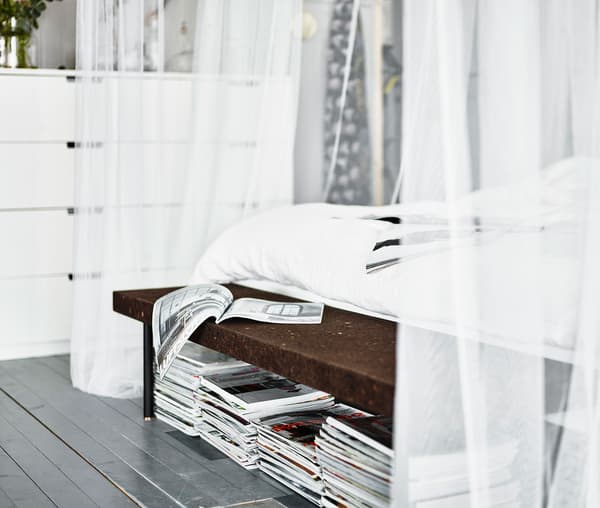 Magazines stacked underneath a cork bench at the end of the bedframe.
