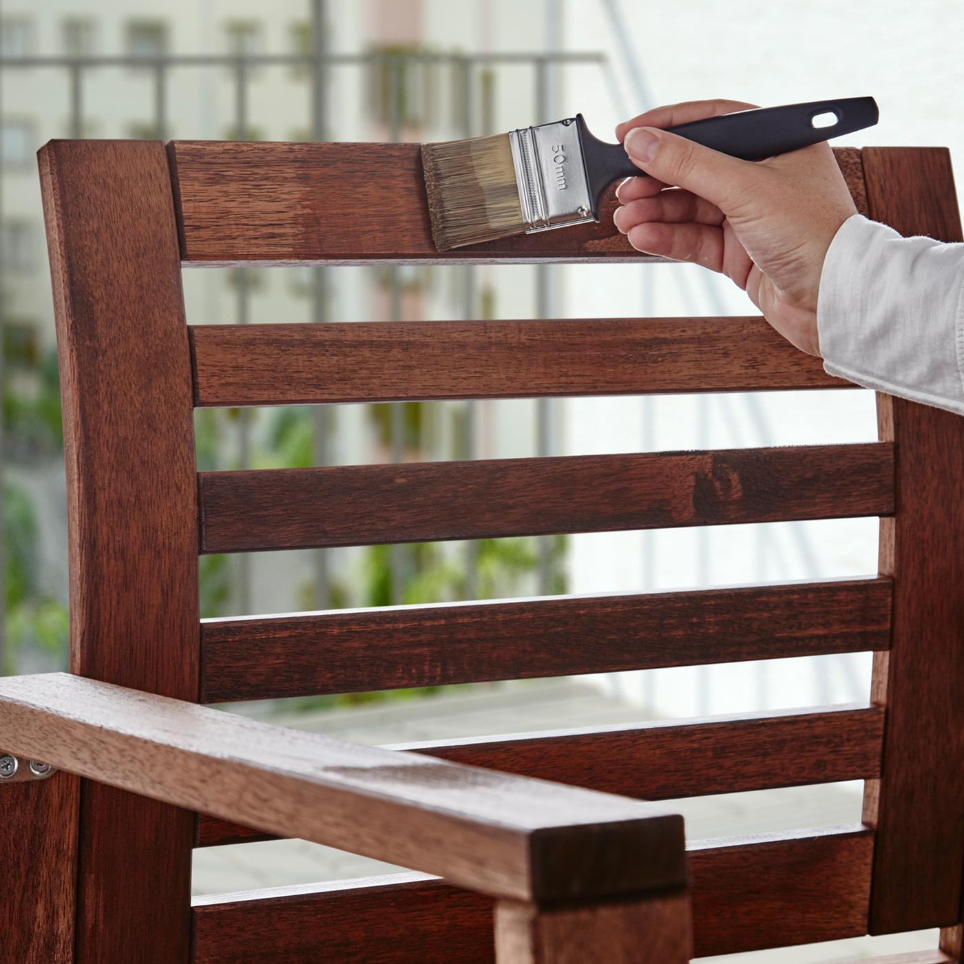 Main appliquant de la lasure VÅRDA sur un fauteuil en bois à l’aide d’un pinceau FIXA.