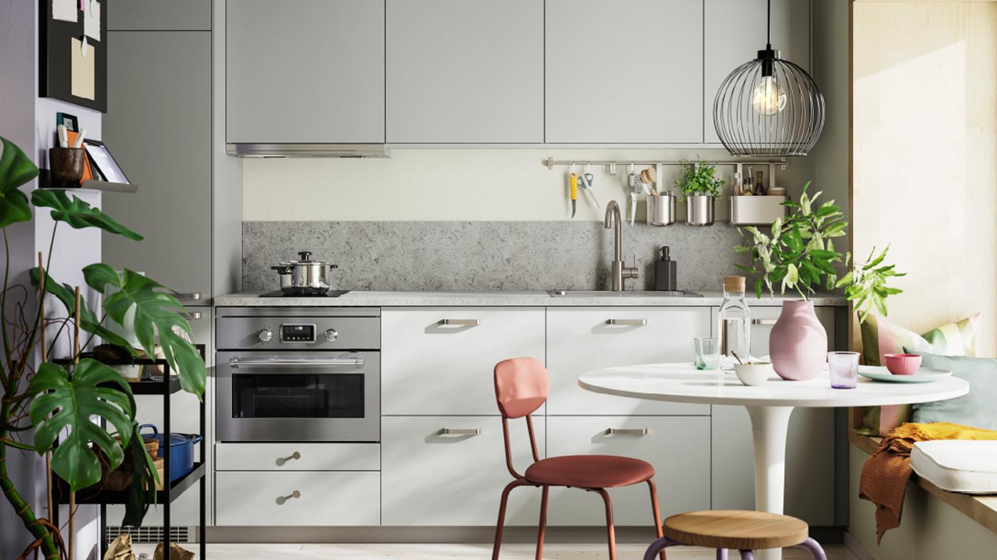 Majhna enovrstna kuhinja s svetlo sivimi HAVSTORP ličnicami, v ospredju pa je pisan jedilni prostor z zelenimi rastlinami.