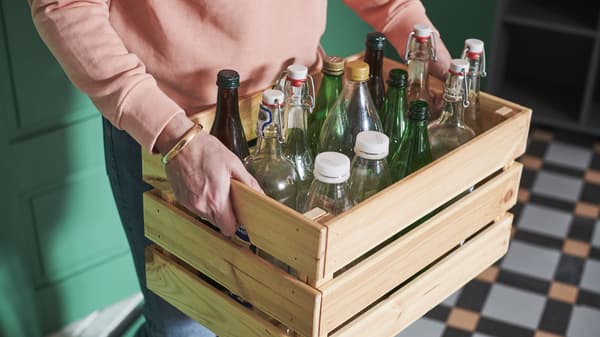 man carrying an IKEA KNAGGLIG crate of glass bottles to be recycled

