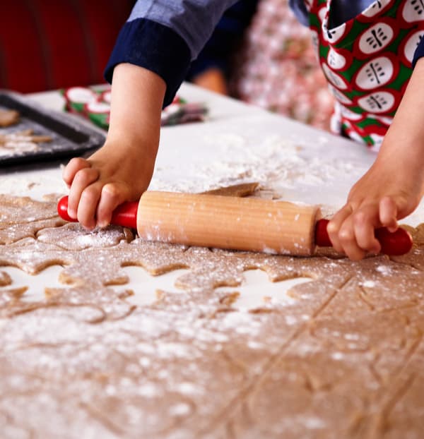 Mani di un bambino che indossa un grembiule e lavora con il mattarello e un po’ di farina l’impasto di pan di zenzero con forme ritagliate - IKEA