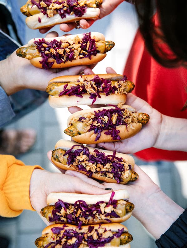 Menschen halten eine Kette von Veggie-Hotdogs in die Höhe.