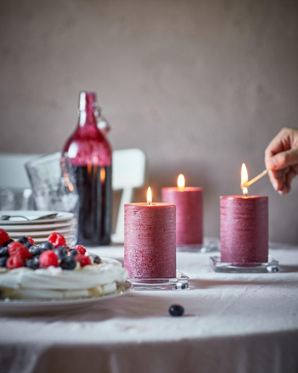 Mesa redonda con tres velones rojos encendidos al lado derecho, al costado izquierdo un plato con frutos rojos