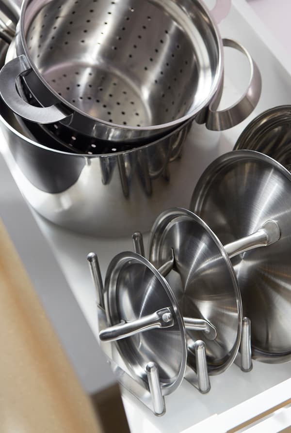 Metal pots and their lids stacked neatly in an open kitchen drawer.