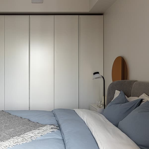 Minimalist bedroom with blue bedding, white wardrobe, and bedside lamp.