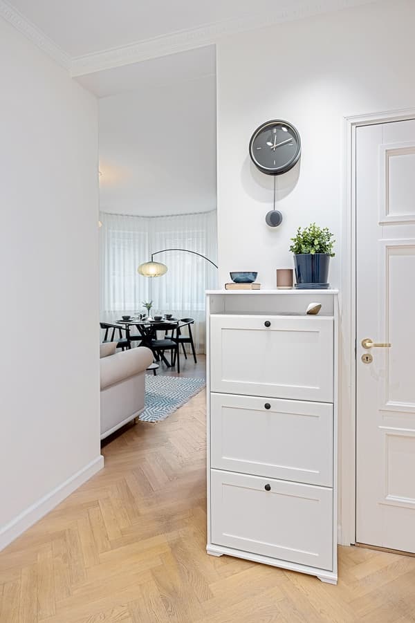 Minimalist hallway with white shoe cabinet, wall clock, and potted plant