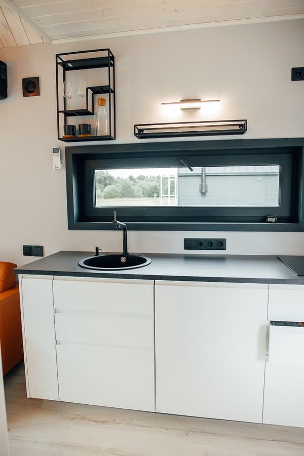 Minimalist kitchen with black round sink and white cabinets – Compact modern kitchen featuring sleek white cabinetry, black countertop, and wall-mounted shelves with glassware.