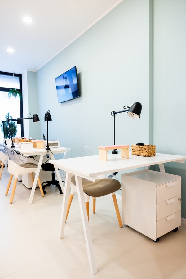 Minimalist nail salon workstations with white desks, black lamps, and comfortable chairs.