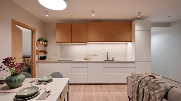 Minimalist open-plan kitchen and dining area with warm wood cabinetry, integrated lighting, soft neutral tones, and contemporary furnishings, creating a bright and welcoming atmosphere for modern living.