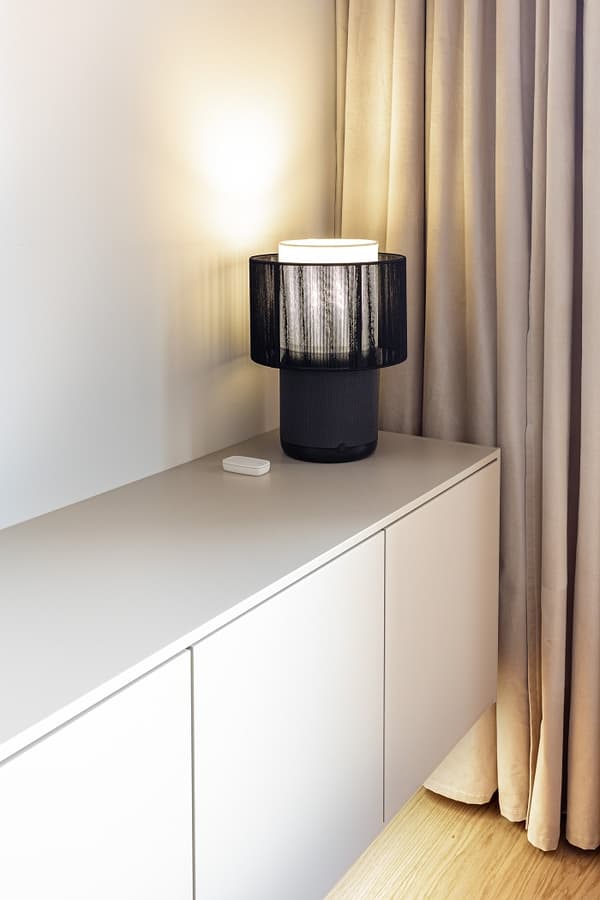 Minimalist sideboard with black table lamp and beige curtains in modern living room.