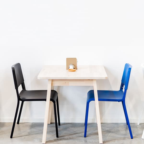 Minimalist small dining table with black and blue chairs in an office break area.
