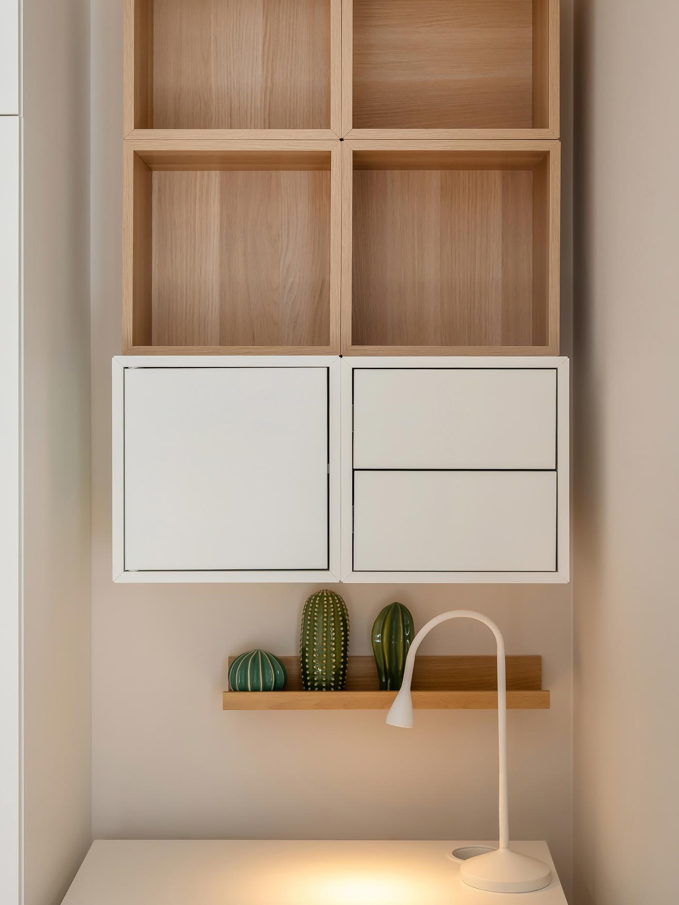 Minimalist workspace with a white desk, lamp, decorative plants, and wall-mounted wooden and white shelving.