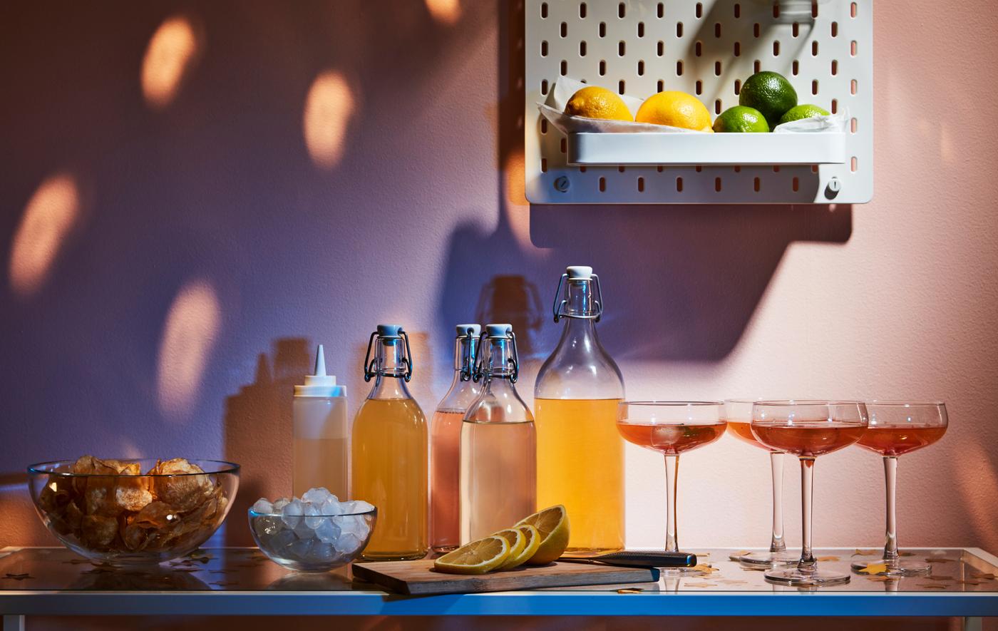 Minuman, gelas dan aksesori dipamerkan di atas meja sisi. Pada dinding di atasnya terdapat papan penyepit SKÅDIS yang mempunyai buah lemon dan buah limau nipis.