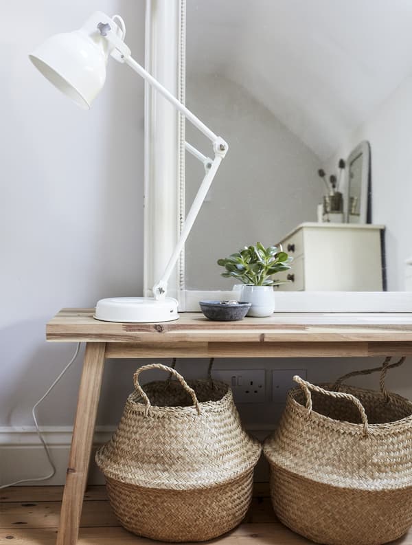 Miroir et lampe posés sur un banc en bois, avec deux paniers de rangement en dessous.
