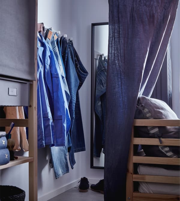 Miroir NISSEDAL et des jeans accrochés à une patère, dans un coin dressing aménagé près du lit.